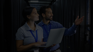 Woman holding a laptop and a man inside a server room